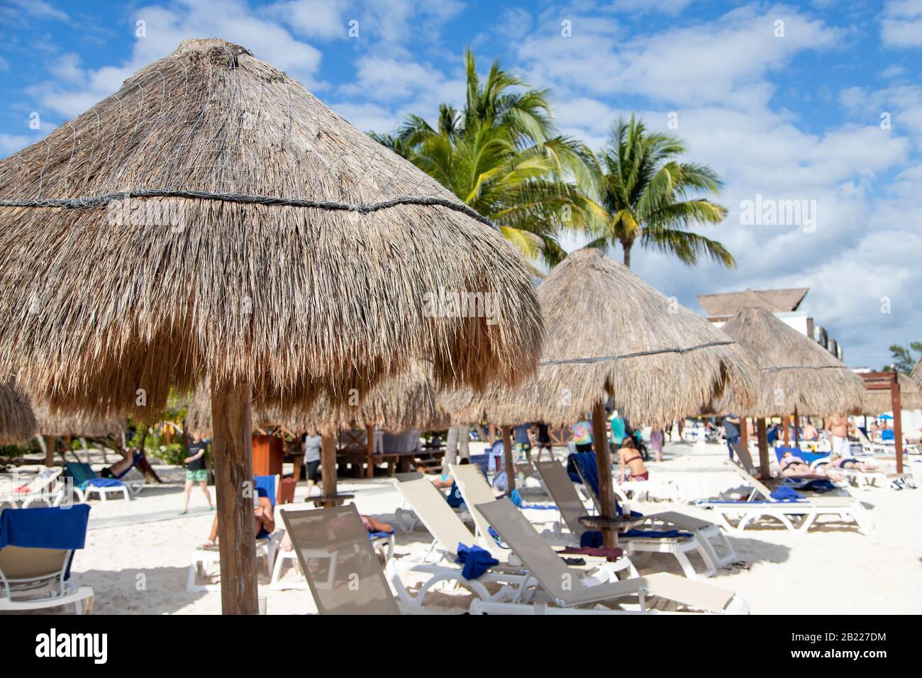 Nahaufnahme des Sonnenschirms mit Kokospalmenblatt und nicht erkennbaren Strandgängern, die sich in einer Entfernung an einem Cancun-Strand an der Riviera Maya in der Karibik entspannen Stockfoto