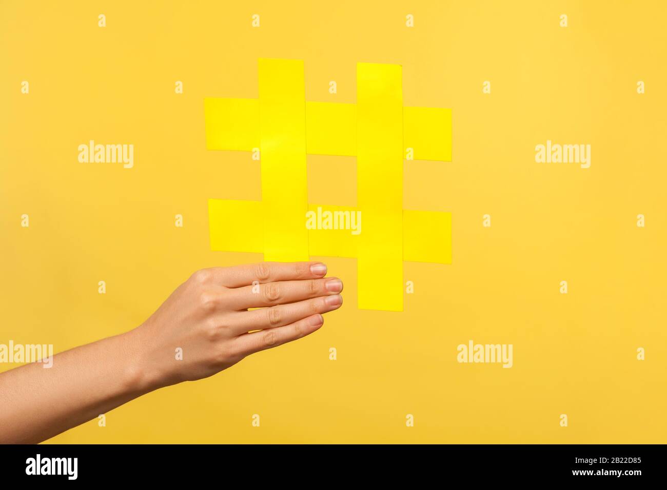 Nahaufnahme der weiblichen Hand, die großes gelbes Hashtag-Symbol für Internettrends, Hash-Zeichen, Blogging und Popularität in sozialen Netzwerken hält. Isolieren Stockfoto