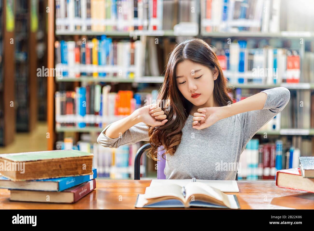 Asian Young Student in Casual Suit Reading und Doing Stretch sich in Bibliothek der Universität oder Colleage mit verschiedenen Büchern und stationären auf dem Holz Stockfoto