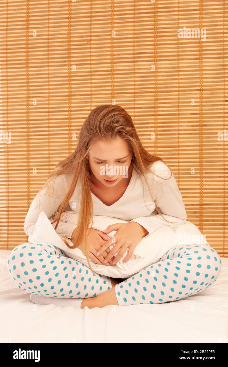 Junge Frau leidet unter Bauchschmerzen, während sie zu Hause auf dem Bett sitzt. Stockfoto