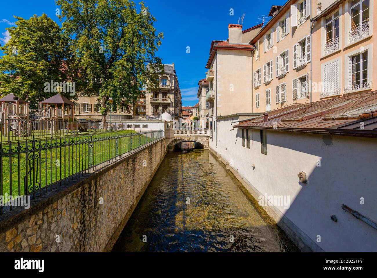 Ein Kanal am Jardin de l'Evêché mit einem Spielplatz in der Nähe von L'église Notre Dame de Liesse gegenüber der Rue Royale Brücke, Annecy, Frankreich im September. Stockfoto