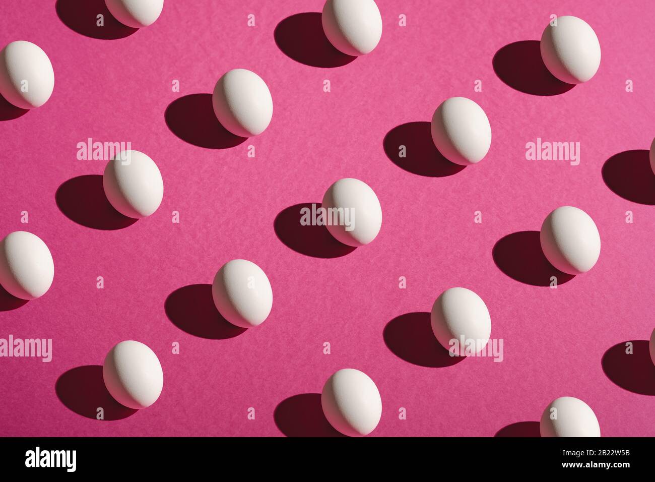 Weiße Eier Muster auf rosa lila Farben schlichter minimaler Hintergrund, Winkelansicht, glücklicher Ostertag Stockfoto