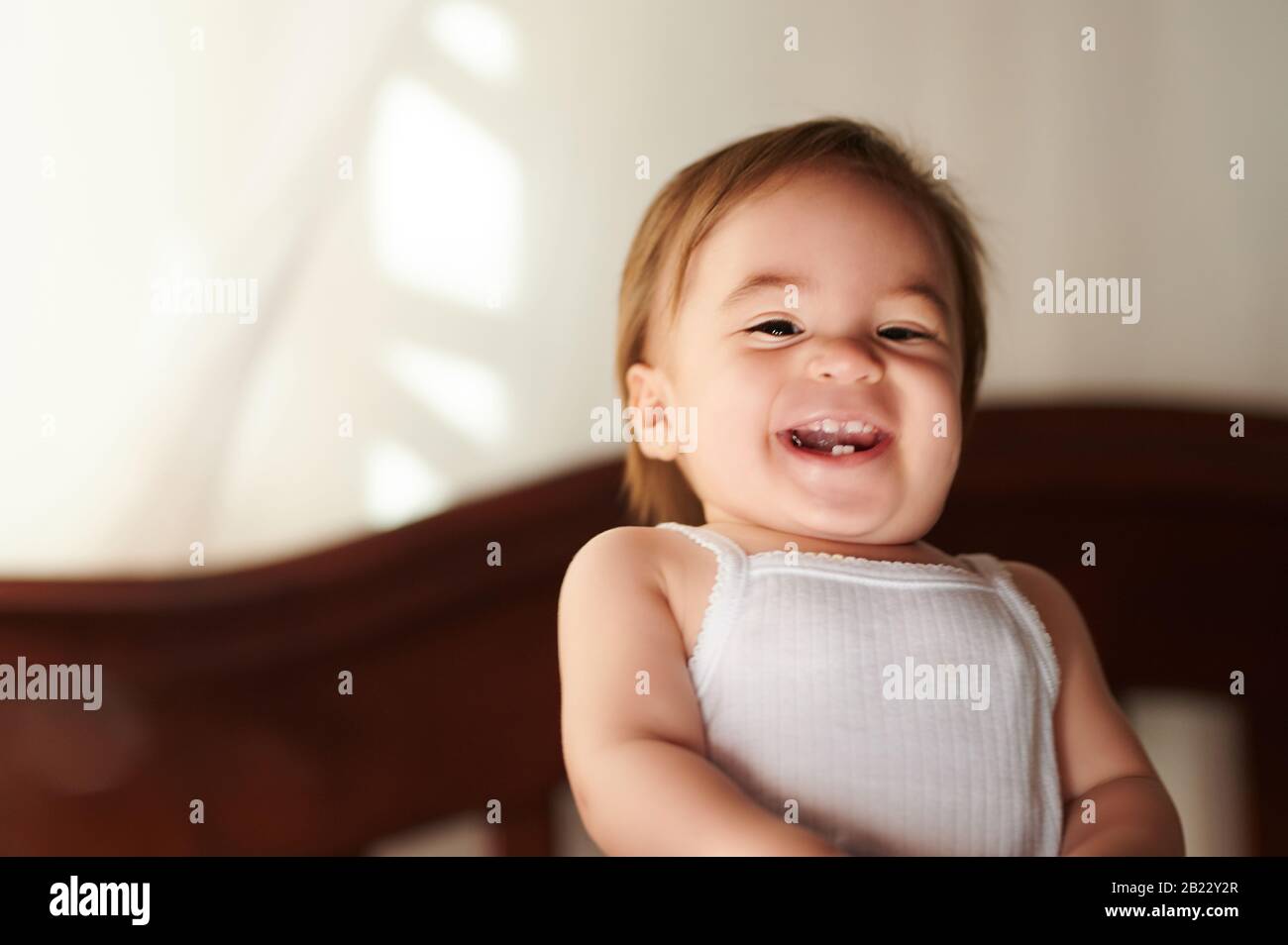 Fröhliches Baby lächelt mit Zähnen auf weißem T-Shirt Stockfoto