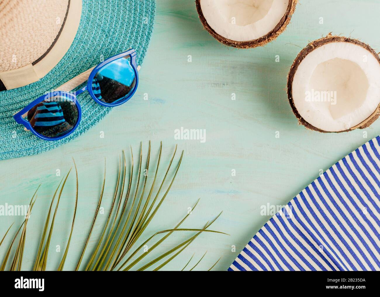 Komposition oder Layout im Sommer. Tropische Palmenblätter, Hut, Brille, Strandtuch, Kokosnuss auf dem Hintergrund von Meeresgrüns. Das Konzept der Sommersaison Stockfoto