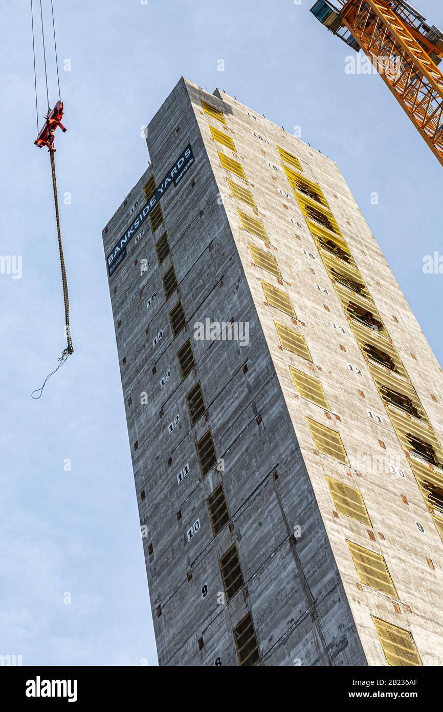 Blick nach oben auf einen 18-stöckigen Betonaufzugsschacht mit einem gelben Turmkran, der das Gebäude umrahmt Stockfoto