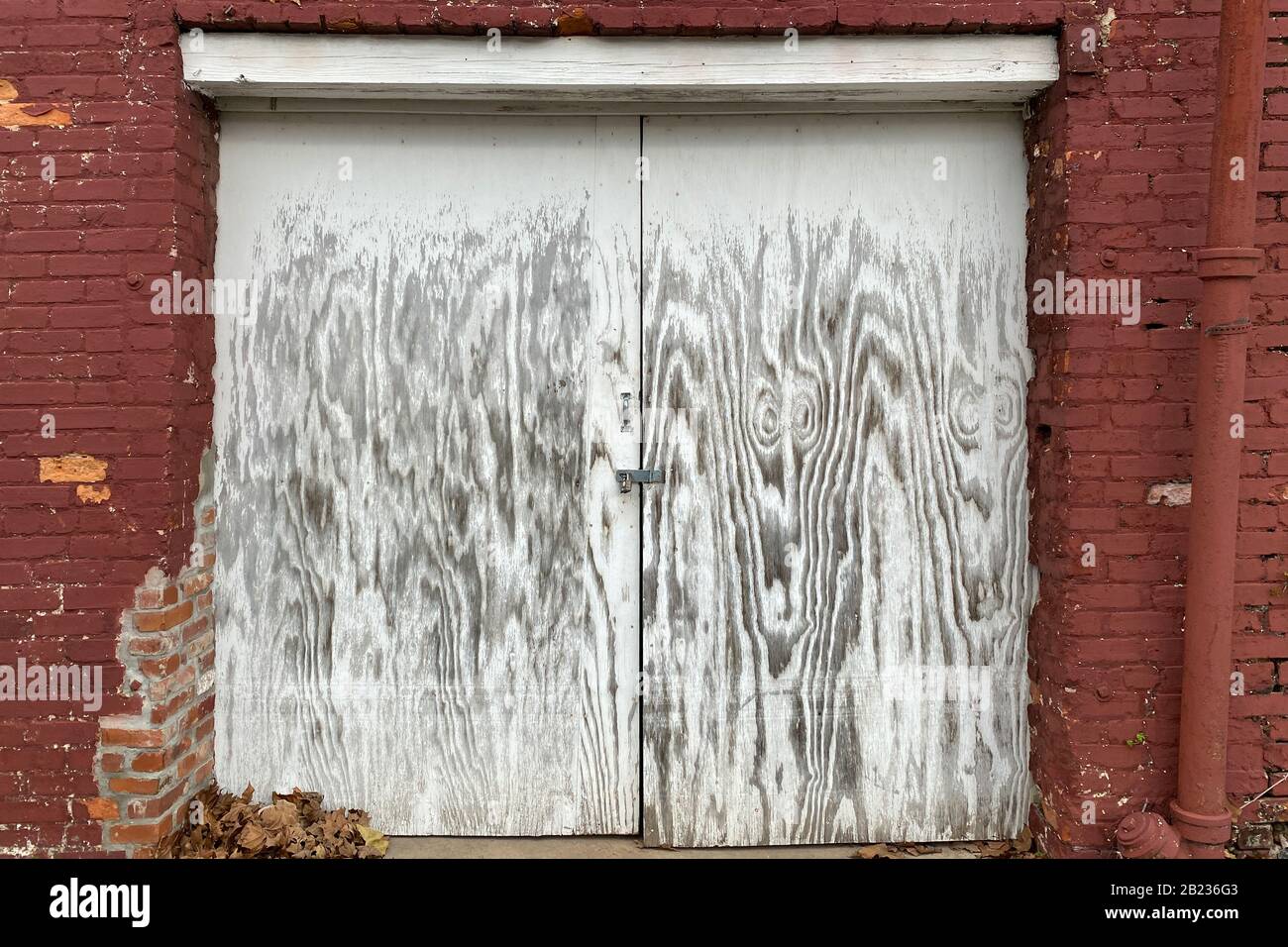 Ein Paar verblichener weiß lackierter verschlossener Versand- und Warenannahme an einem roten Backallee-Lagerhaus Stockfoto