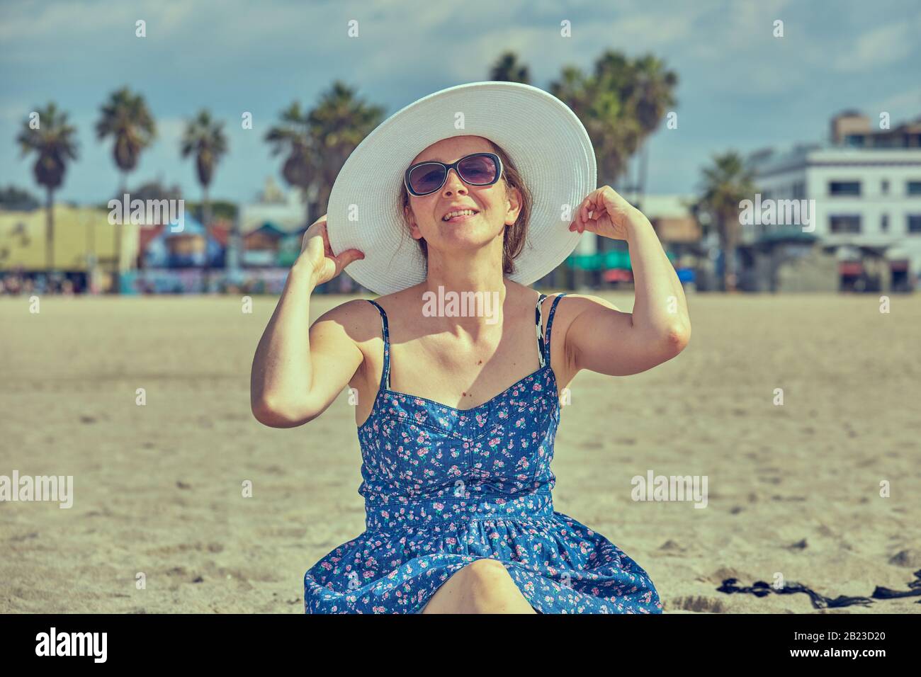 Junge Frau mit klassischer blauer Sonnenkresse, weißer Sonnenhut und Sonnenbrille an einem kalifornischen Strand Stockfoto