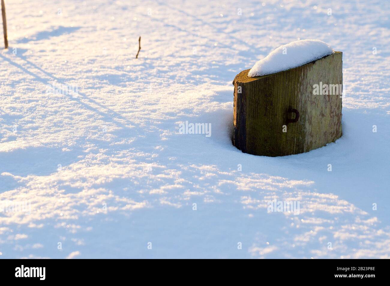 Nahaufnahme eines schneebedeckten Fenkeposts, der durch die Spitze einer Schneeverwehung stochte, die von einer niedrigen warmen Wintersonne angezündet wird. Stockfoto