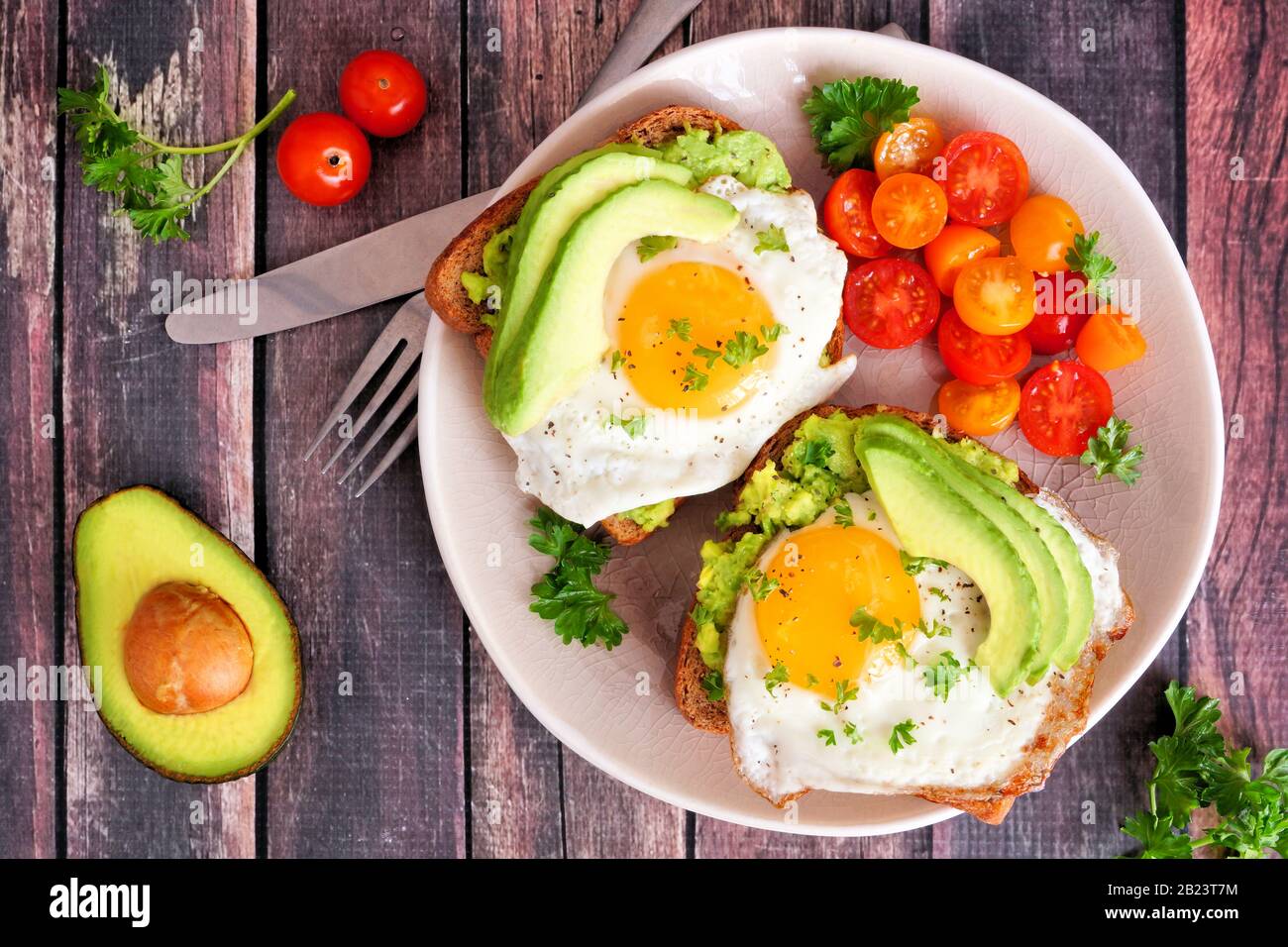 Avocado-Toast mit Eiern und Tomaten auf Vollkornbrot. Über dem Blick auf einen dunklen Holzhintergrund. Stockfoto