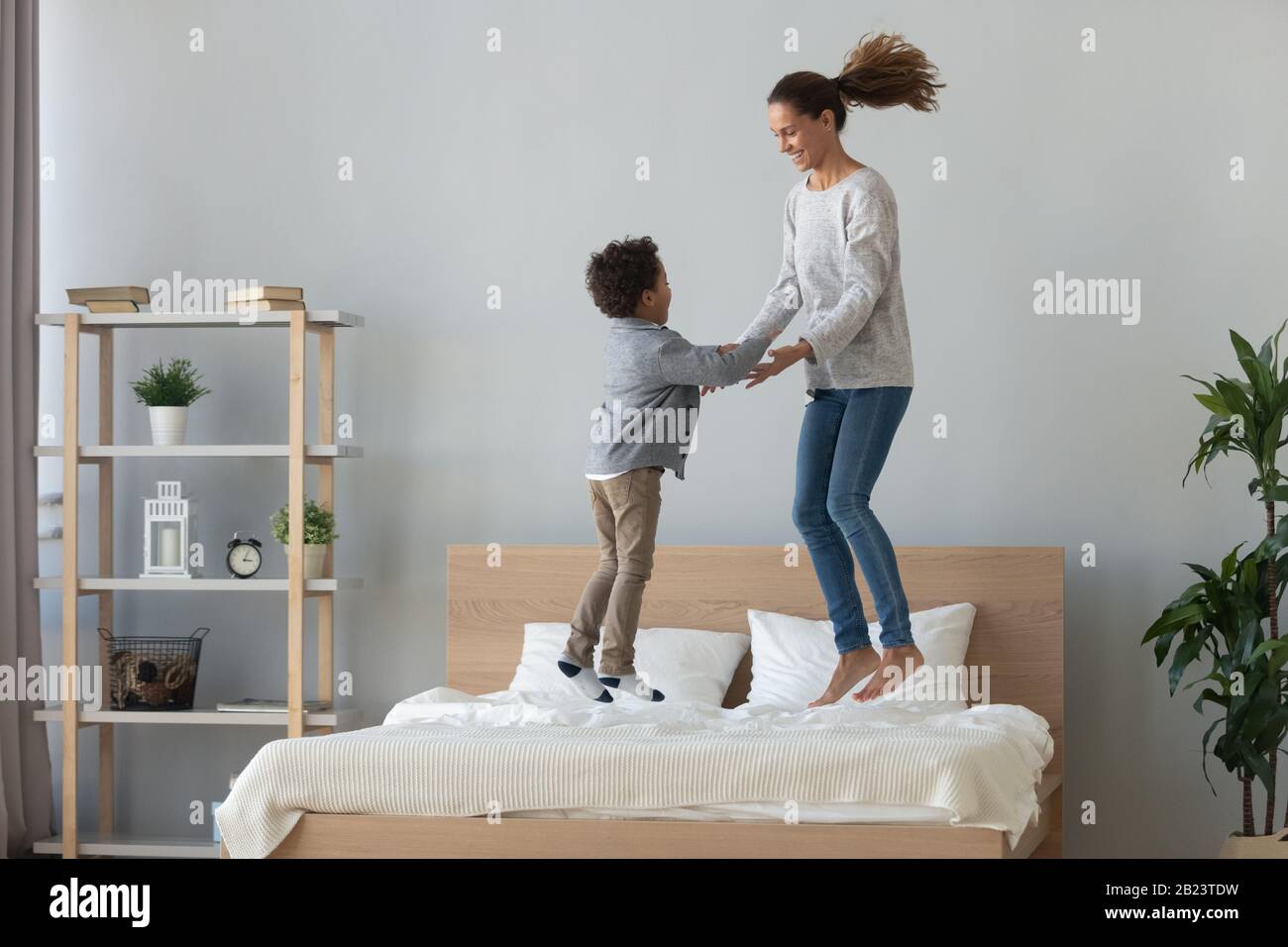 Fröhliche gemischte Rasse Mutter und kleiner Sohn springen auf dem Bett Stockfoto
