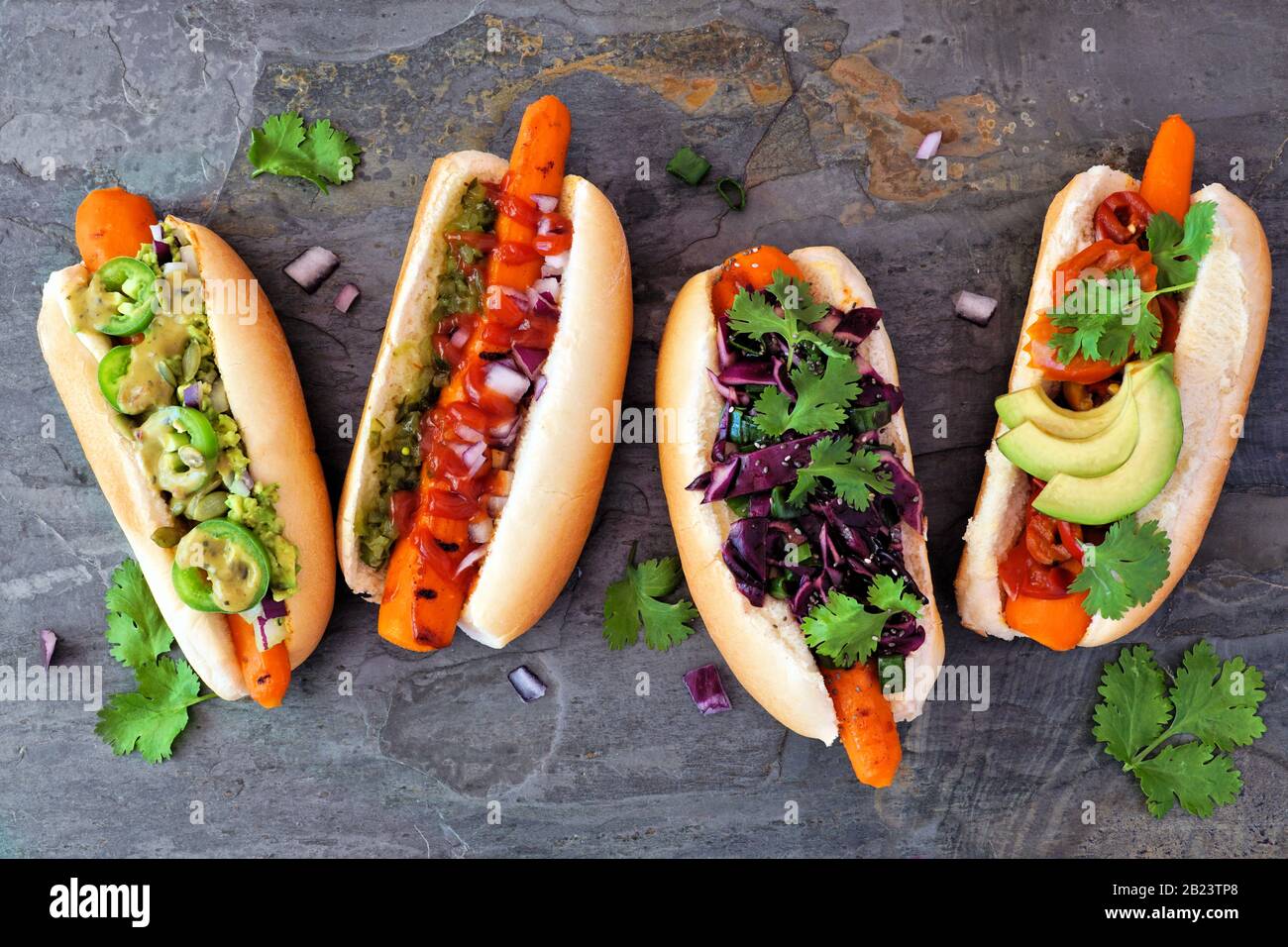 Karotten vegane Hot Dogs mit verschiedenen Belägen. Über der Bildfläche auf dunklem Schieferhintergrund. Pflanzliches, fleischloses Essenskonzept. Stockfoto