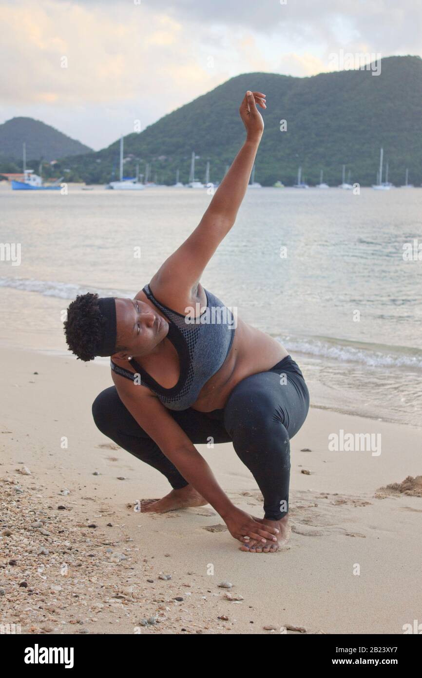 Afrikanische Dame mit Naturhaar Training Stretching am Strand trägt einen Sport-BH und schwarze Strumpfhosen brennen Bauch Fett und bleiben fit und gesund Stockfoto