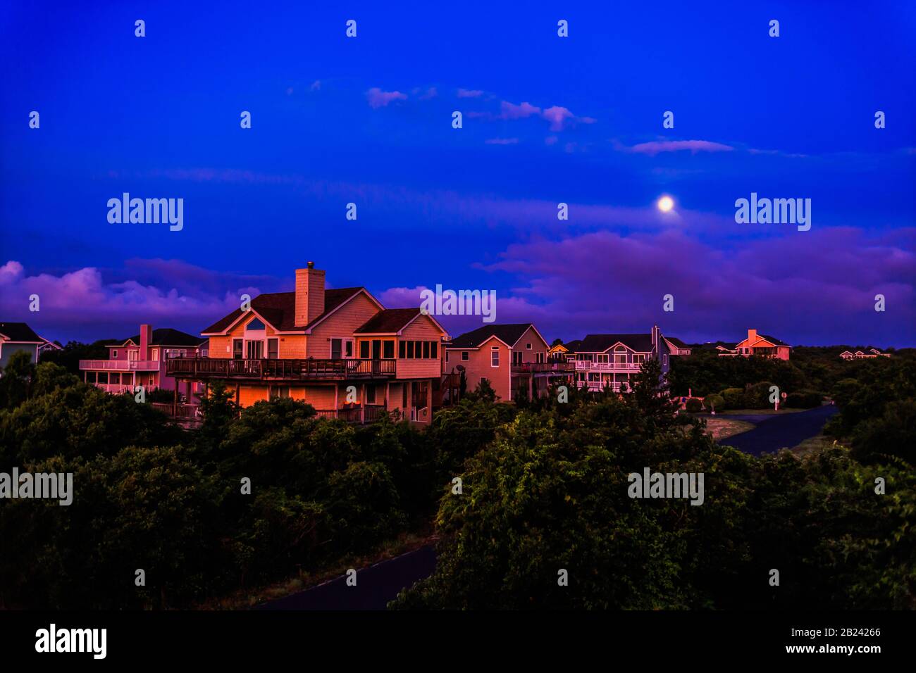 Erste Strahlen der Morgendämmerung leuchten auf den Ferienhäusern an der Küste gegen einen verblassenden Nachthimmel und Mond. Stockfoto