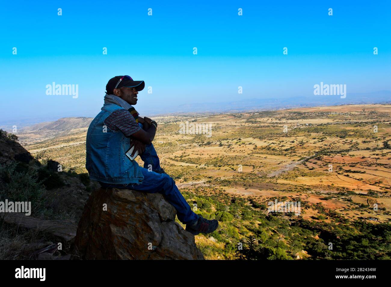 Der junge Mann aus der Region thront auf einem Felsen mit Blick auf die Landschaft der äthiopischen Highlands, Hawzien, Tigray, Äthiopien Stockfoto