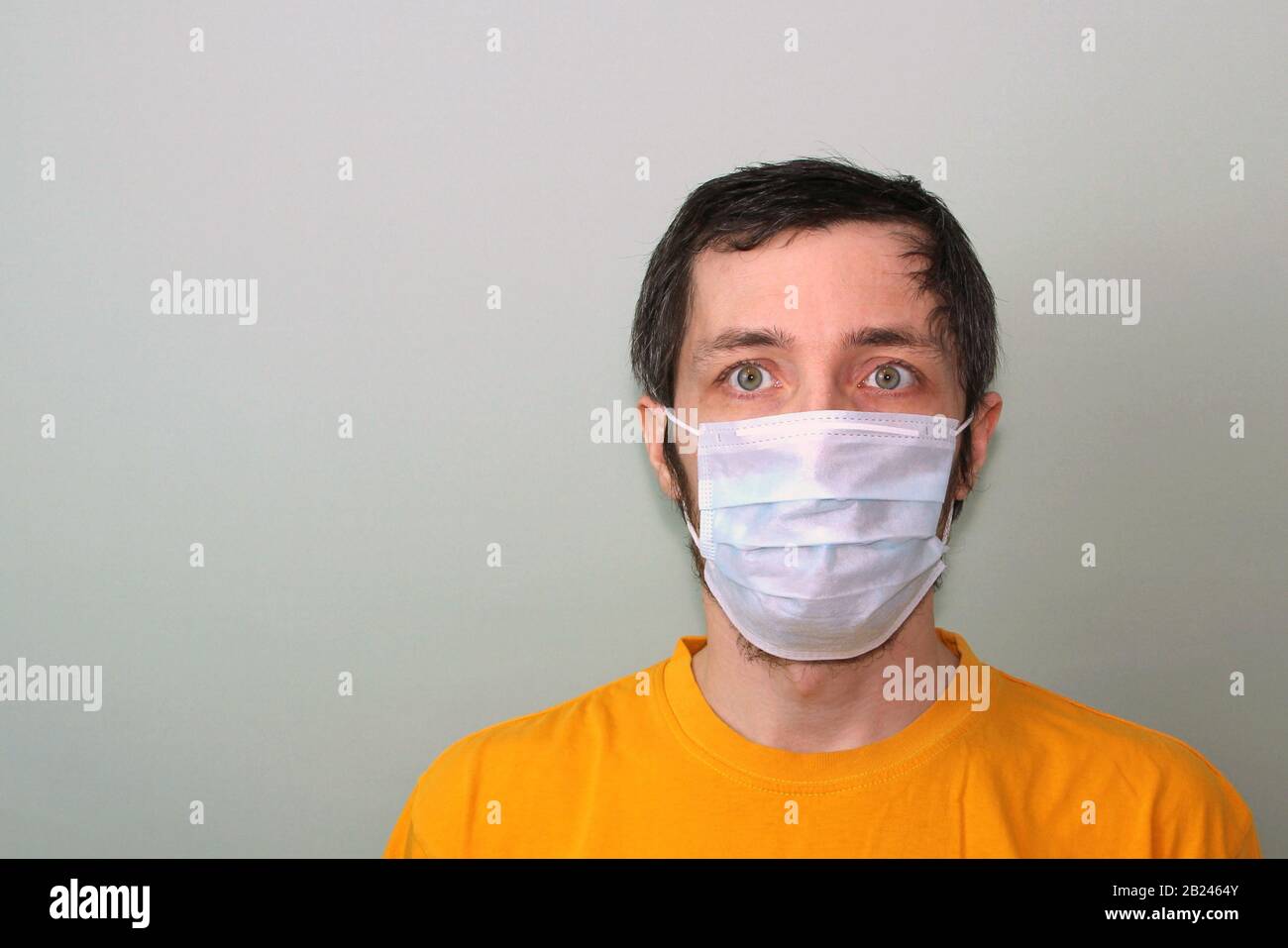 Erwachsener mittleren Alters in einem gelben T-Shirt auf grauem Hintergrund in einer medizinischen Maske. Krankheitsschutz Coronavirus epidemisches Problem aus China. Stockfoto