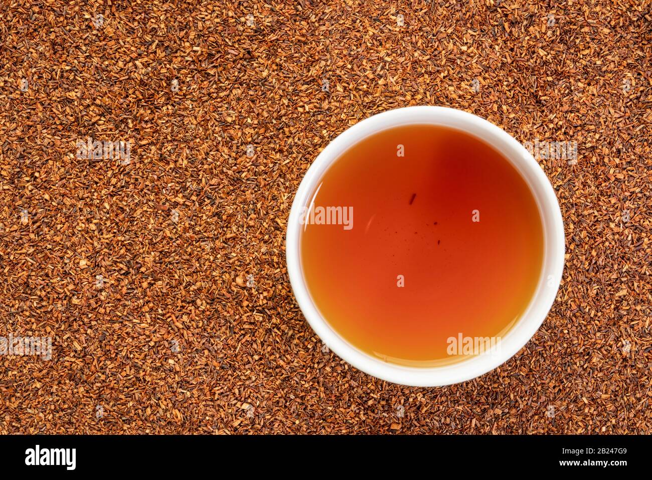 Rooibos roter Tee - eine weiße Tasse heißen Getränks gegen Backgroiund aus lockeren Blättern, Tee aus dem südafrikanischen roten Busch, natürlich koffeinfrei Stockfoto