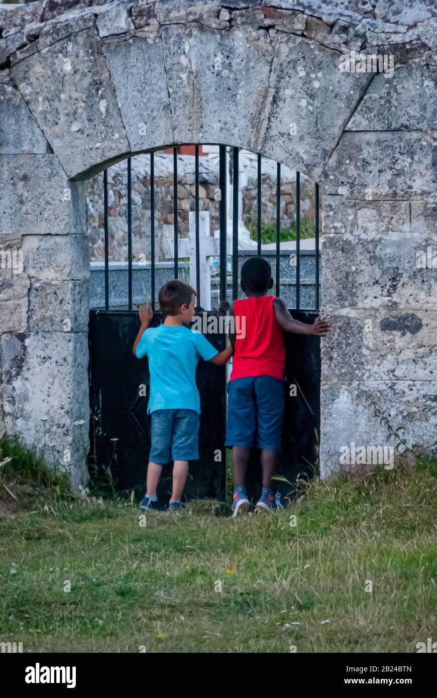 Weißer Junge und schwarzer Junge, der durch die Friedhofstür blickt Stockfoto