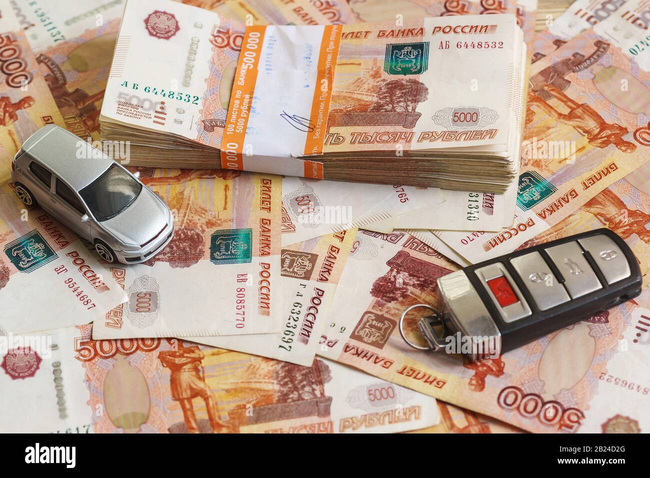 Das Fünf-Tausendstel-Rubel-Paket in einer halben Million russischen Rubel, silbernes Modellauto und der Zündschlüssel stehen vor dem verstreuten Verbot Stockfoto