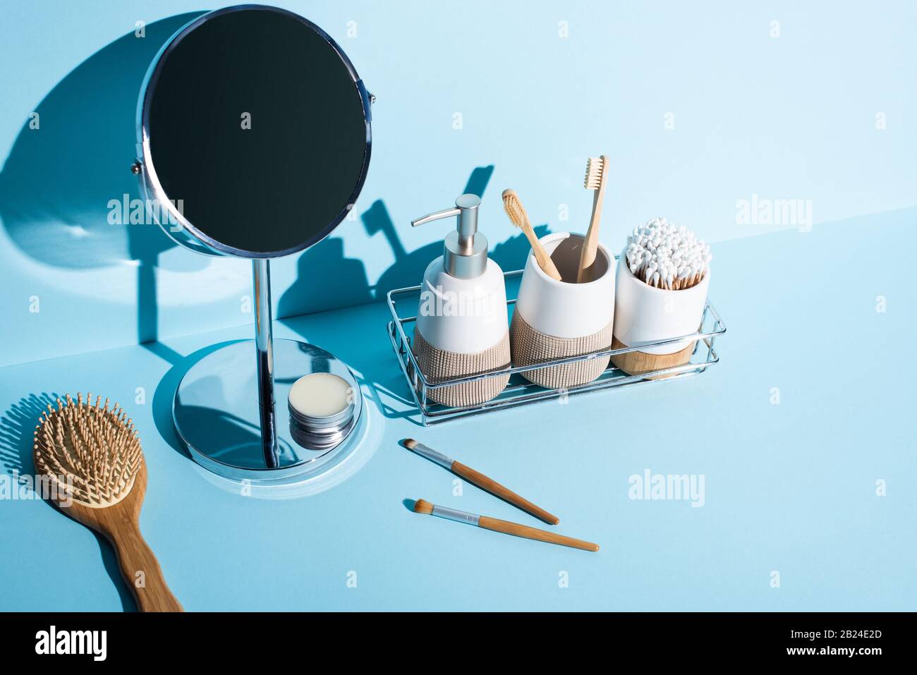 Zahnbürstenhalter mit Hygieneartikeln, Spender im Badregal mit Spiegel, Haarbürste, Kosmetikbürsten auf blauem Hintergrund, Entsorgungskonzept Null Stockfoto