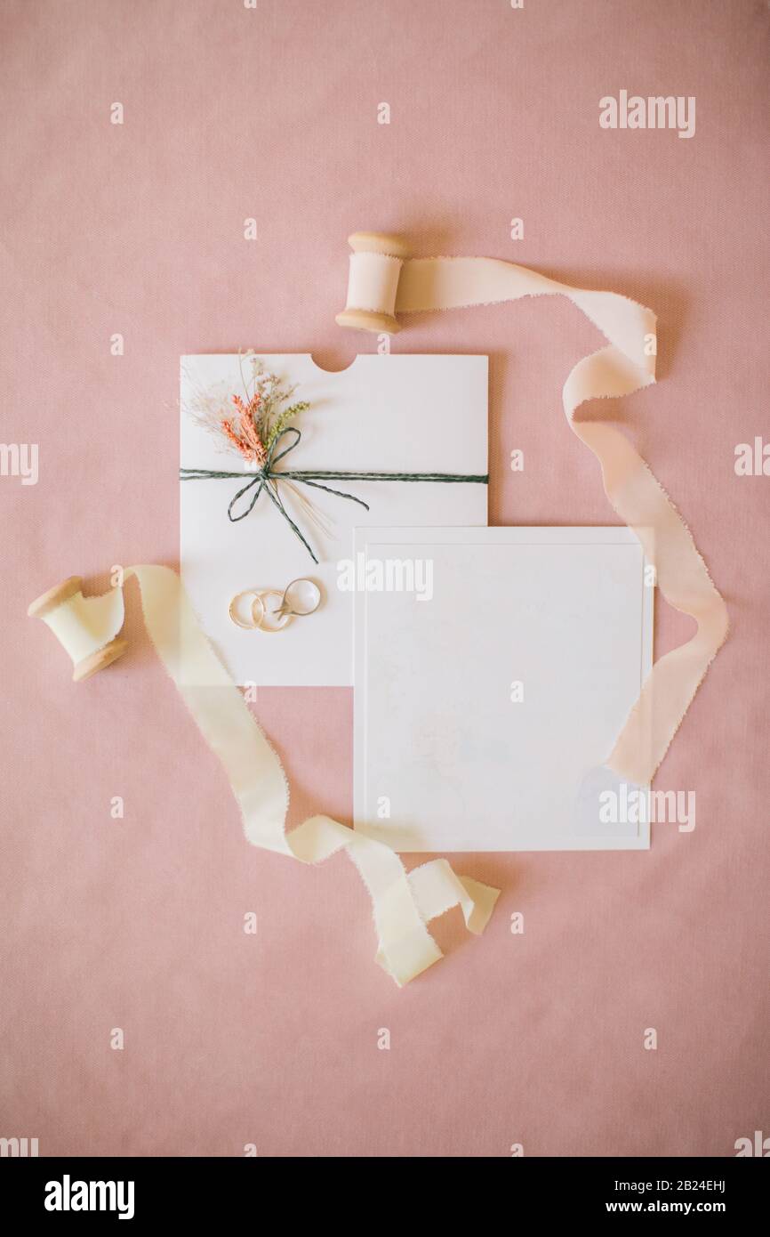 Hochzeitseinladung im rosa Hintergrund. Seidenstoffrollen, Diamantringe und Hochzeitsringe. Stockfoto