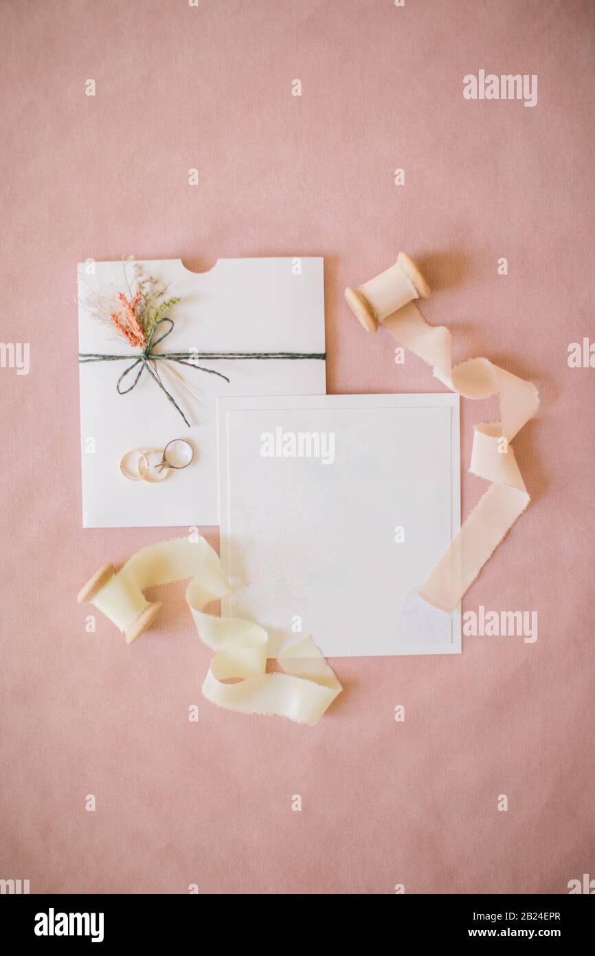 Hochzeitseinladung im rosa Hintergrund. Seidenstoffrollen, Diamantringe und Hochzeitsringe. Stockfoto