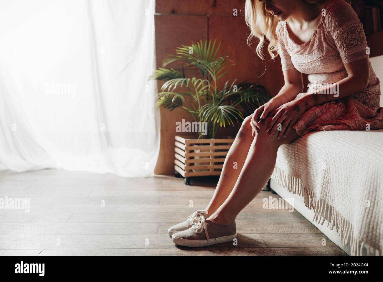 3/4-Ansicht der Frau, die mit Prellungen das Knie berührt, während sie auf dem Sofa sitzt Stockfoto