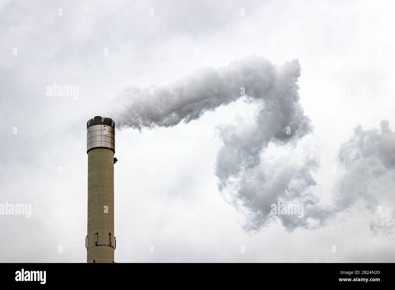 Hoher Schornstein, der Gase in die Atmosphäre abgibt und Luftverschmutzung verursacht. Grauer, bewölkter Himmel. Stockfoto