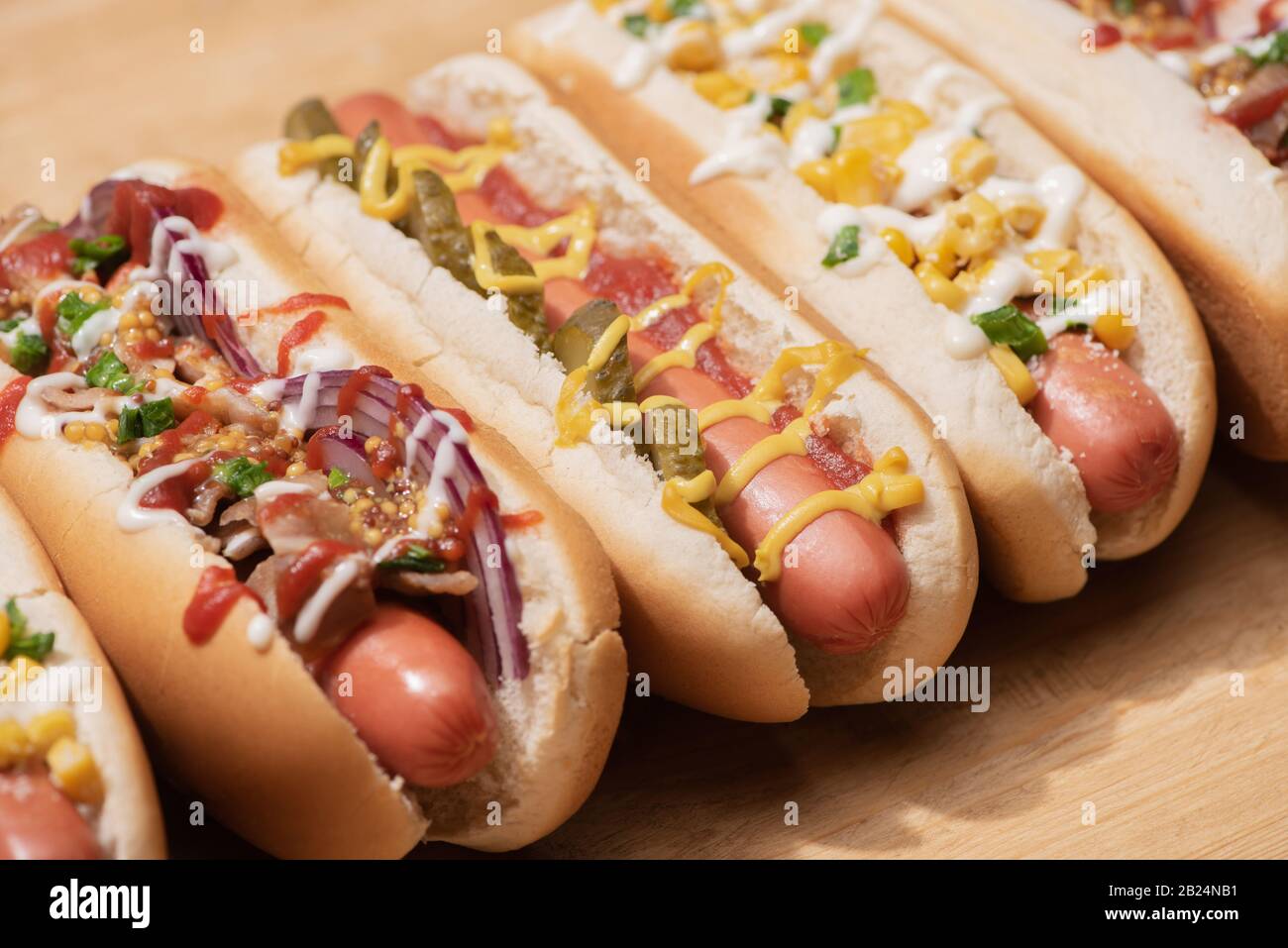 Verschiedene köstliche Hot Dogs mit Gemüse und Soßen auf Holztisch Stockfoto