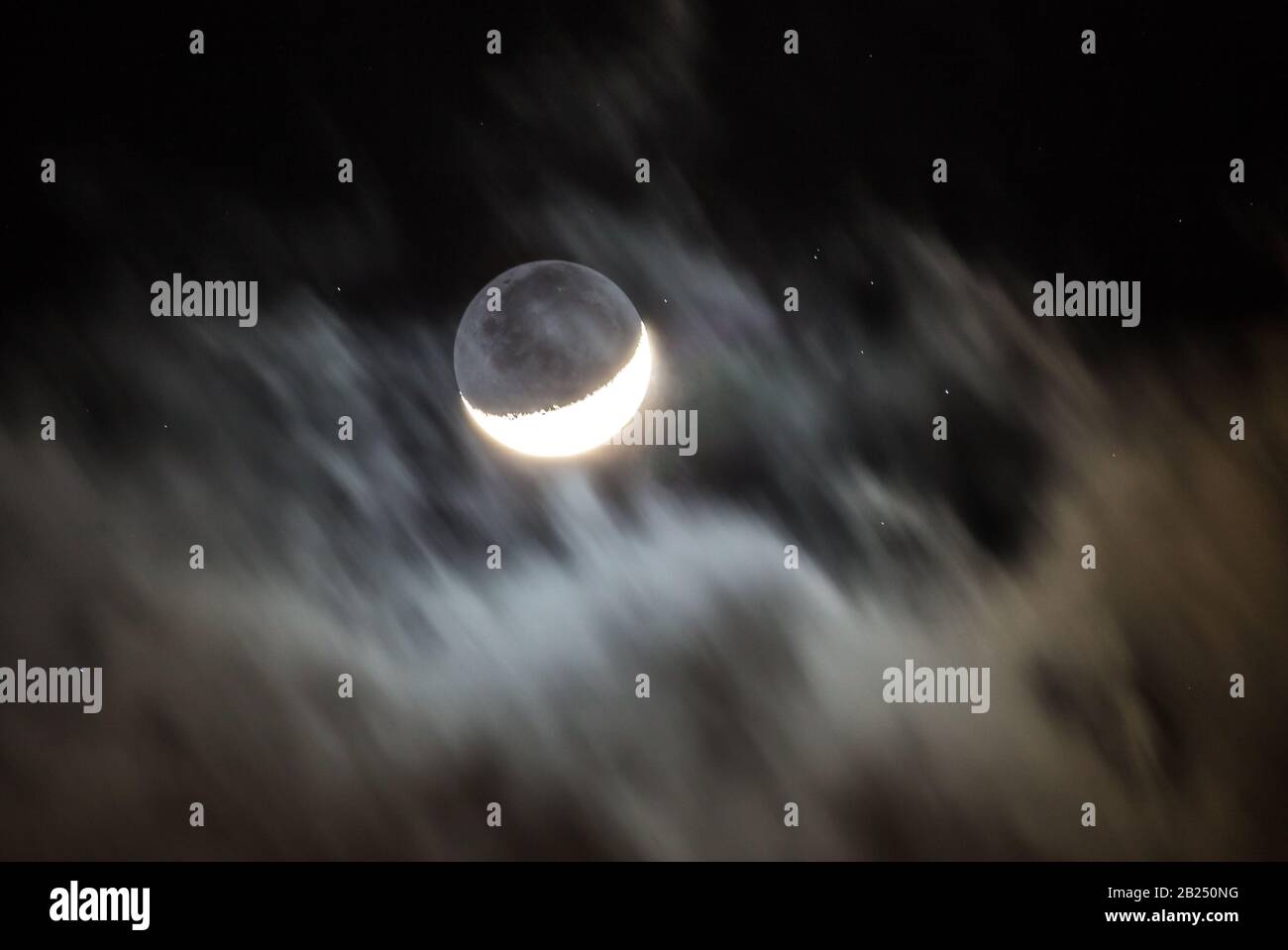 Ein Halbmond wird von schnell vorbeiziehenden Wolken umrahmt, während Sterne in einem schwarzen Himmel darüber hinaus leuchten. Stockfoto