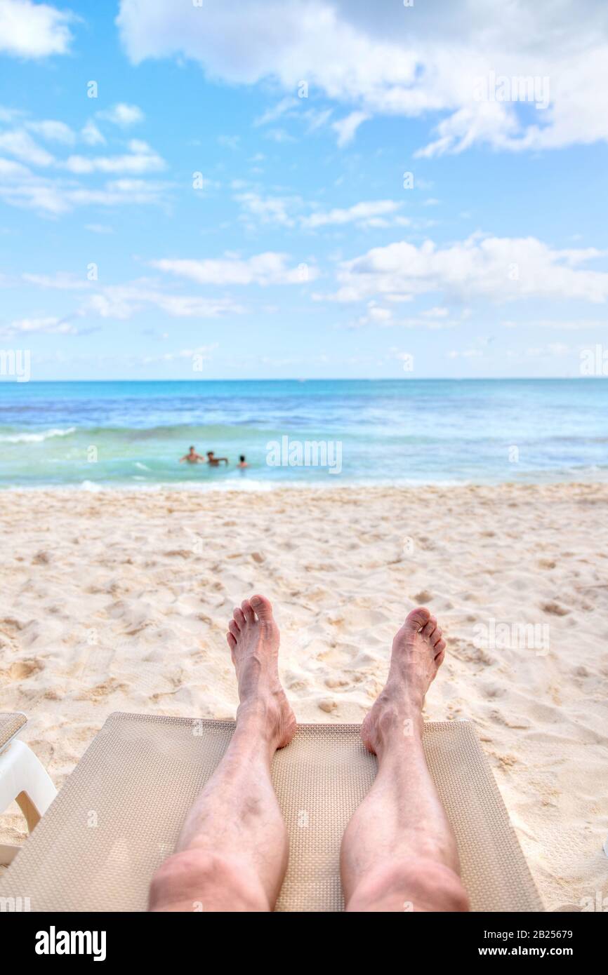 Persönliche Perspektive des Menschen auf einem Liegestuhl am sandigen Strand mit Fußblick auf das Meer und Kopierraum. Aufnahme in den Caribbean coas Stockfoto