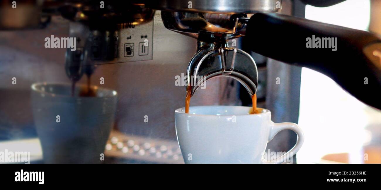 Ein Banner in Computergröße zeigt, dass Espresso von einer Espressomaschine in eine weiße Tasse tropft. Stockfoto