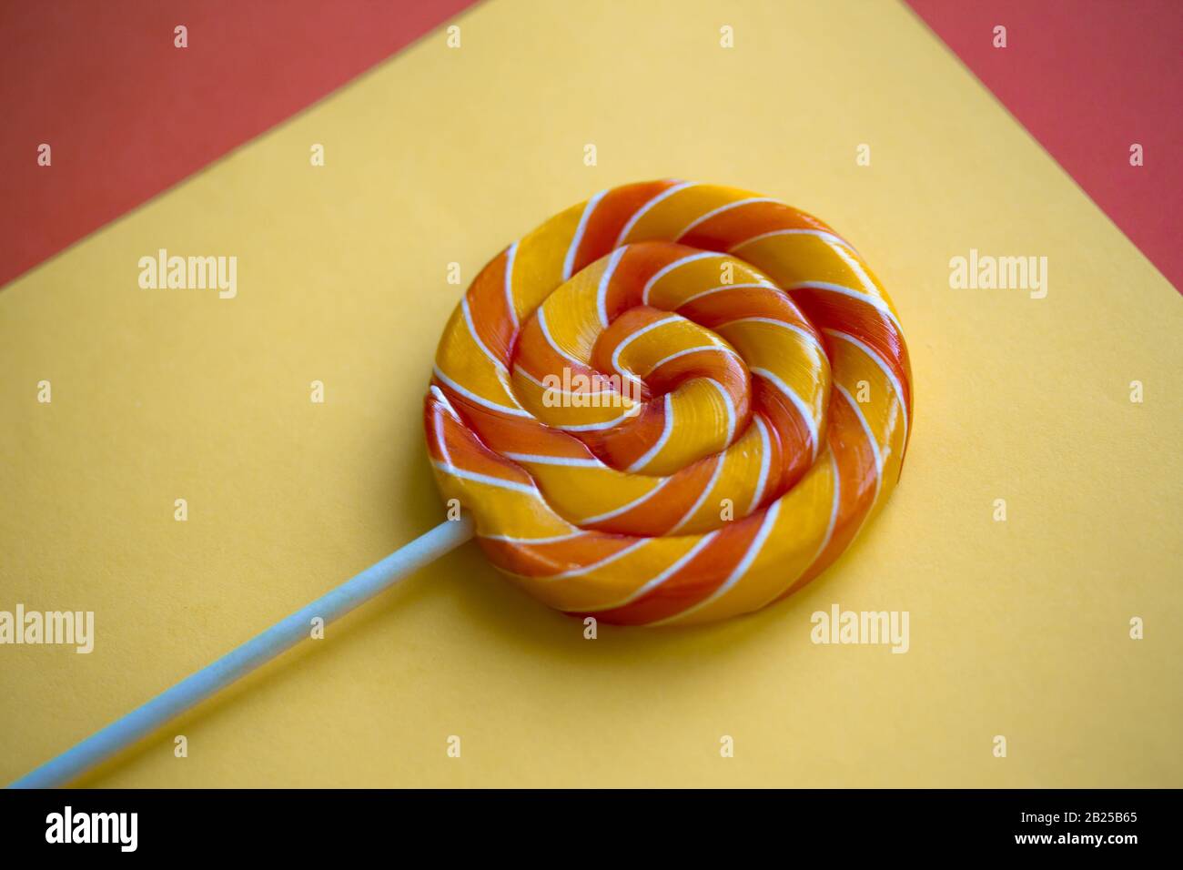 Helles Drall-Lollipop auf gelbem und orangefarbenem Hintergrund. Festlicher Hintergrund mit bunter verdrehter Süßigkeit. Nahaufnahme des Regenbogens rund süß auf Stock. Stockfoto