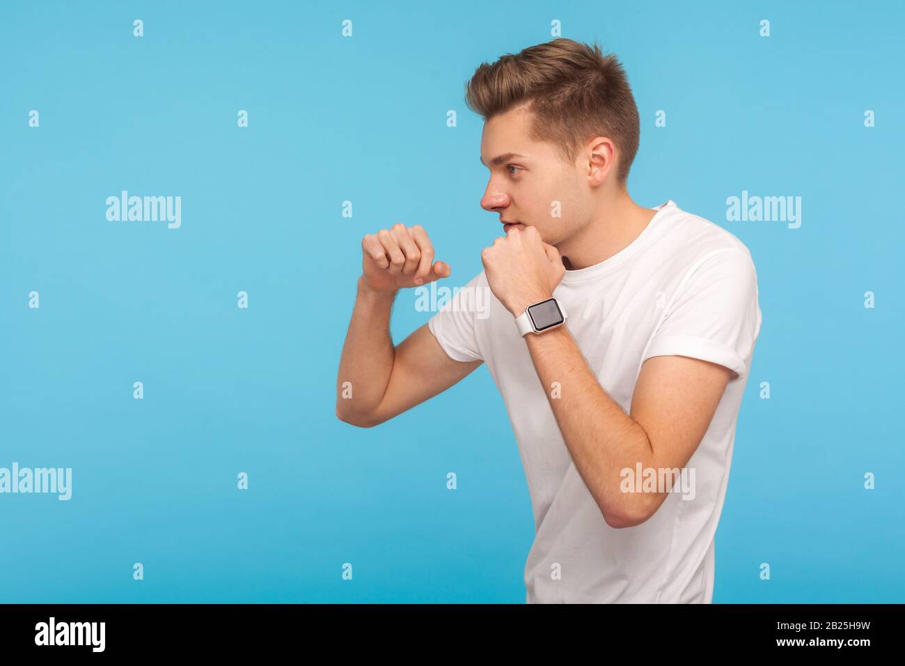 Kampfgeist. Profil des aggressiven Mannes in weißem T-Shirt, der Fäuste in Boxgeste knistert und mutig auf Seite schaut, bereit zu stanzen, zu kämpfen. I Stockfoto