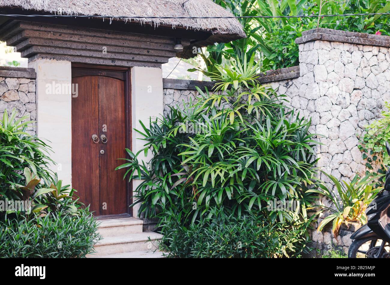 Blick auf die Haustür in einem von grünen Pflanzen umgebenen Steinzaun. Wohnvilla in den Tropen. Bali, Indonesien Stockfoto
