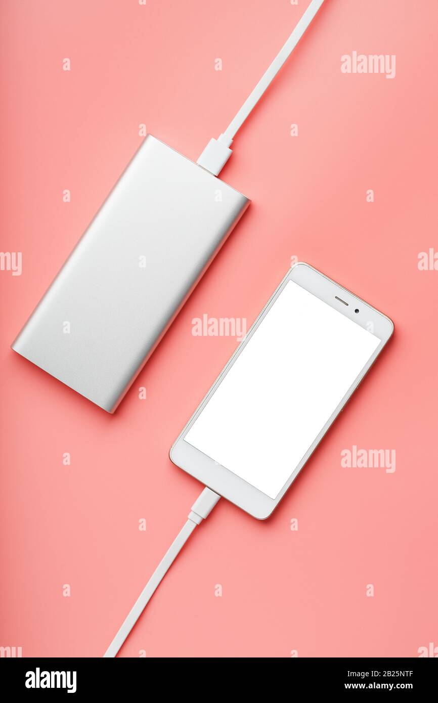 Power Bank lädt Ihr Smartphone auf einem rosafarbenen Hintergrund auf. Universeller externer Akku für Gadgets, freier Speicherplatz und minimalistische Komposition. Tragbares Zeichen Stockfoto