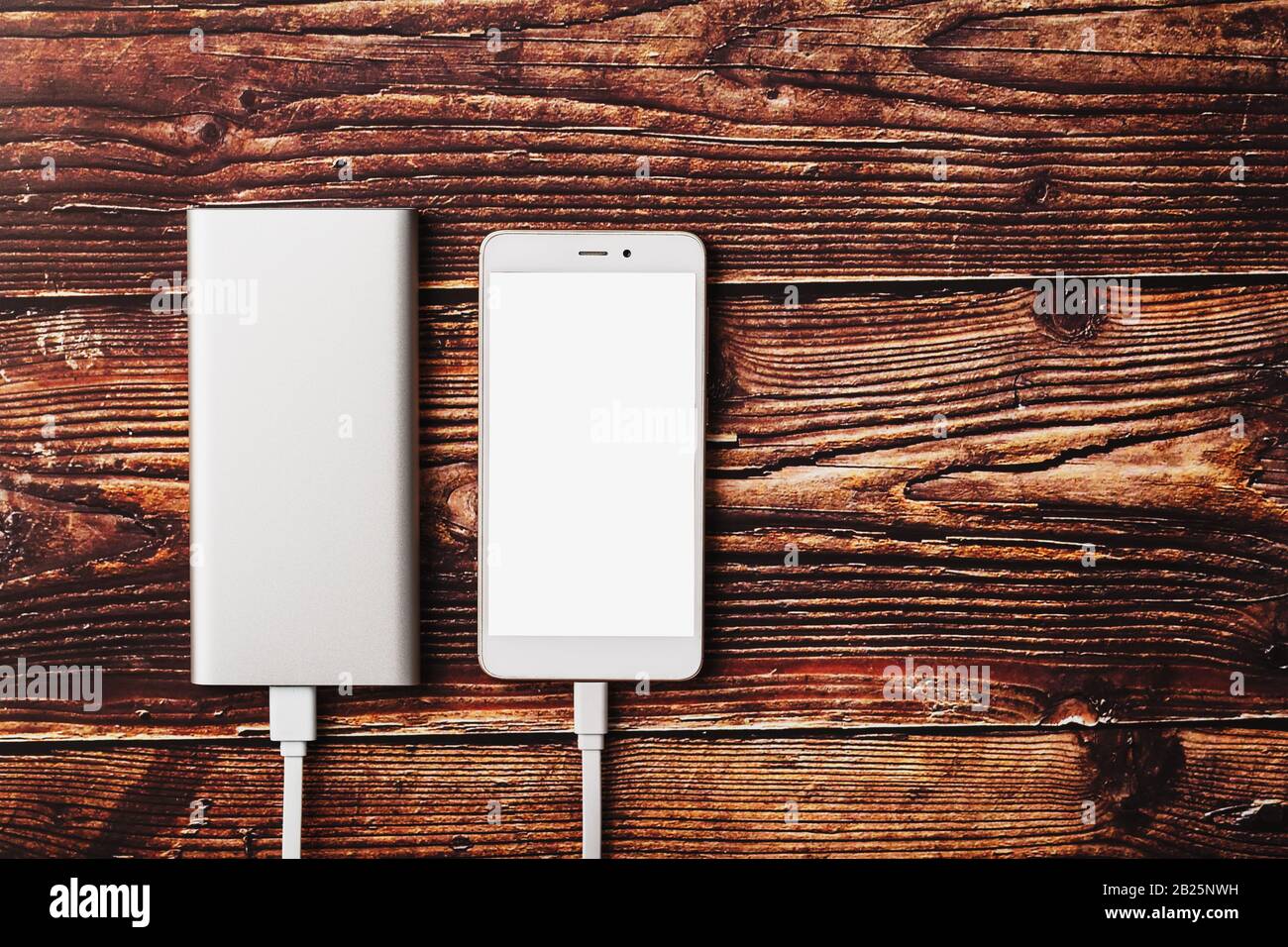 Power Bank lädt ein Smartphone auf einem Holzhintergrund auf. Universeller externer Akku für Gadgets Freier Platz und minimalistische Komposition. Stockfoto