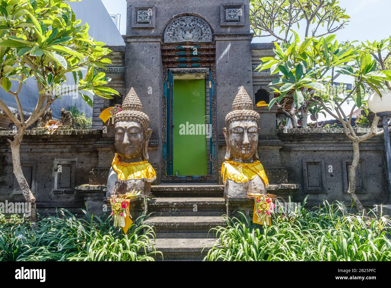 Steinstatuen aus zwei Buddha-Köpfen in goldenem "prada"-Stoff in der Nähe eines traditionellen balinesischen Hauses in Desa Munggu, Bali, Indonesien. Stockfoto