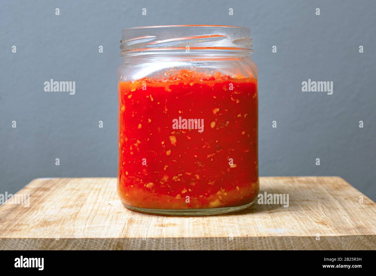 Glas mit Sauce Adjika aus Tomaten, Chili und süßen Paprika auf einem Holztisch grauer Hintergrund. Stockfoto