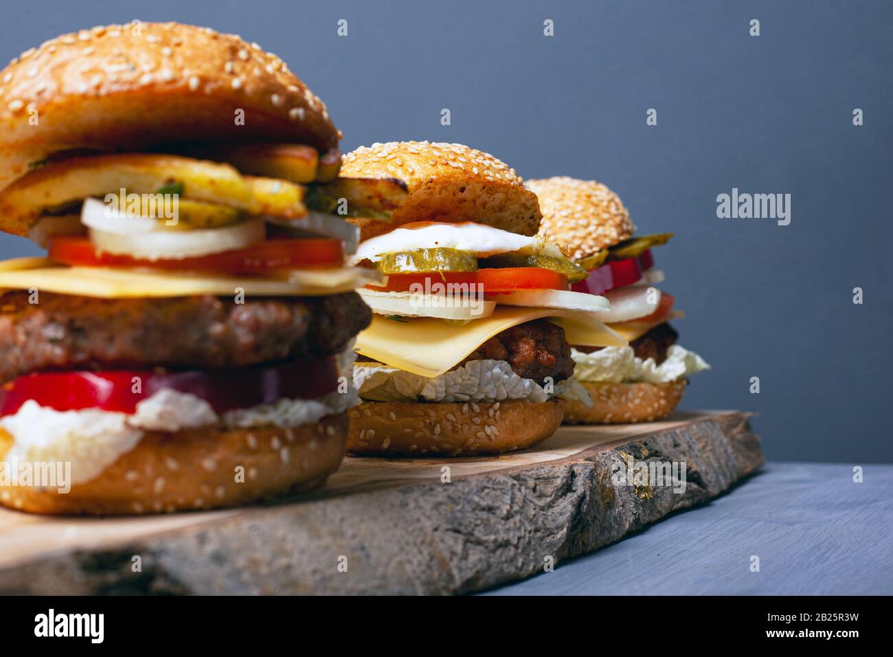 Drei Burger auf einem Holzwald stehen auf grauem Grund. Herzhaftes Mittagessen.Nahaufnahme. Stockfoto