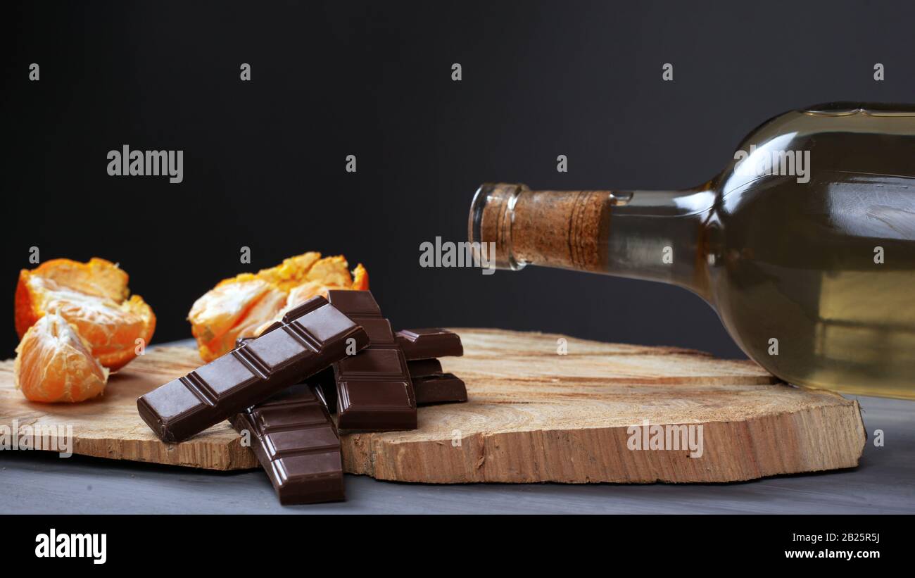 Flasche Weißwein mit Milchschokolade und Tangerine auf einem Holzständer auf dunklem Hintergrund. Romantisches Abendessen für zwei nahe- Stockfoto