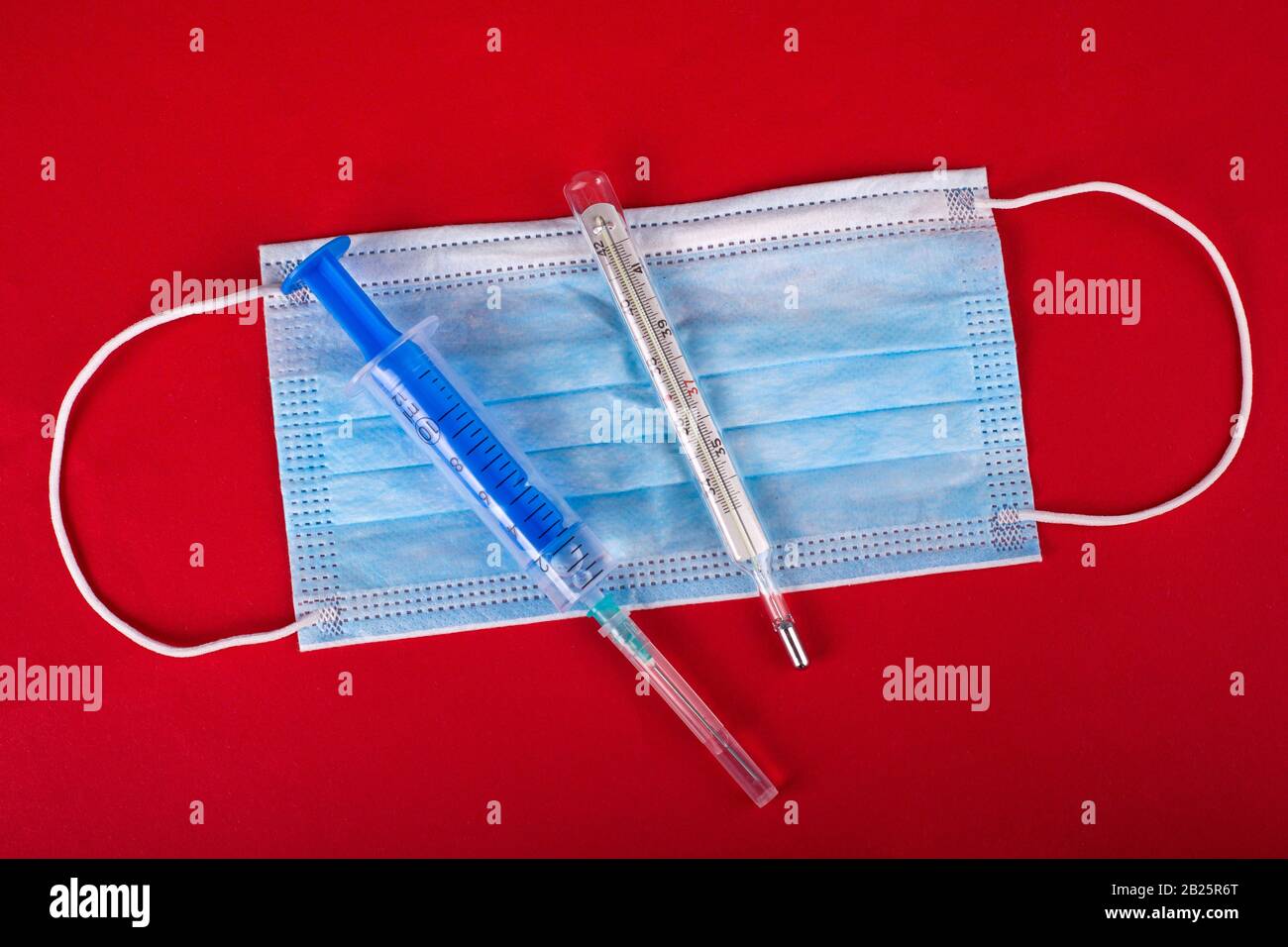 VORSICHTSMASSNAHMEN für die virale Infektion mit Coronavirus, Kovid-2019. Medizinisches Schutzmasken-Thermometer und Spritze mit einem Impfstoff auf rotem Hintergrund. Stockfoto