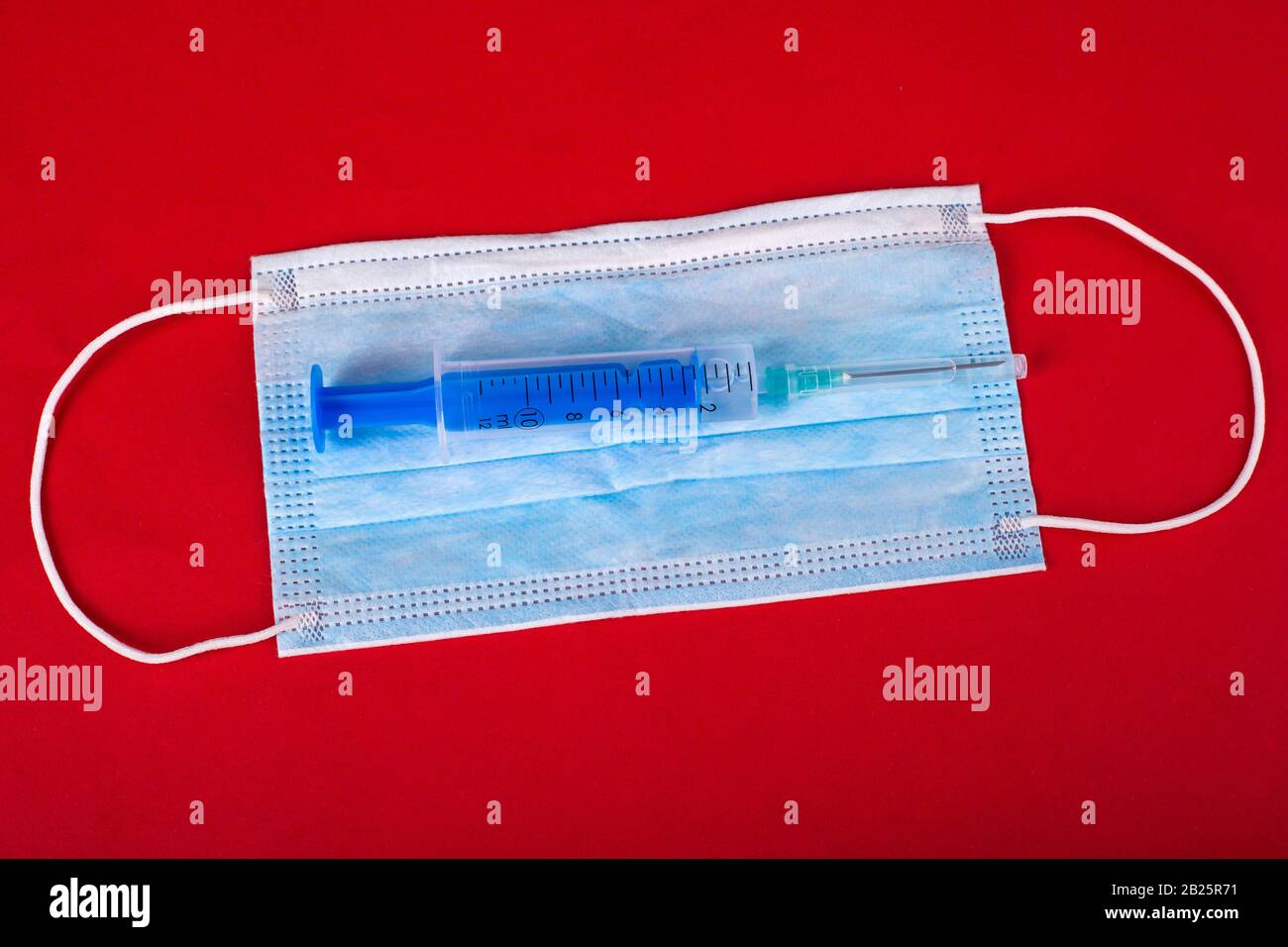 VORSICHTSMASSNAHMEN für die virale Infektion mit Coronavirus, Kovid-2019. Blaue medizinische Schutzmaske und Spritze mit einem Impfstoff auf rotem Hintergrund. Stockfoto