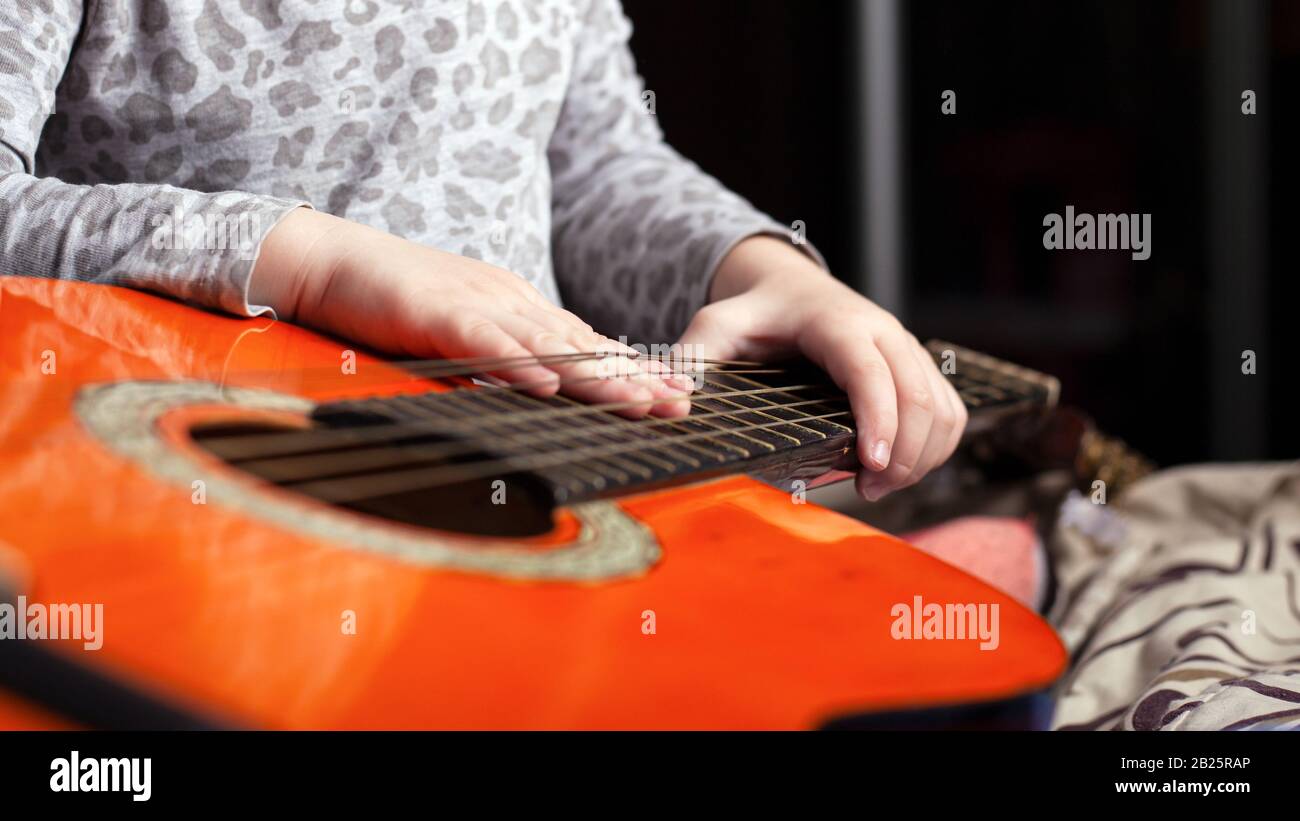 Ein Kind spielt eine akustische sechssaitige Gitarre in oranger Farbe. Stockfoto