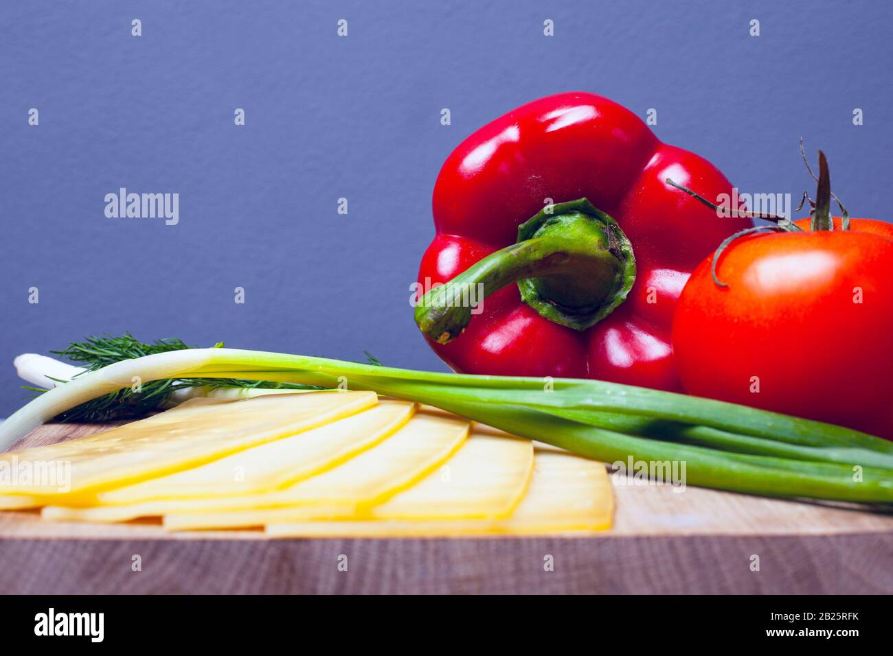 Gemüse mit Kräutern und Käse. Auf einem Holzständer auf grauem Grund. Paprika Tomate und grüne Zwiebel. Nahaufnahme. Stockfoto