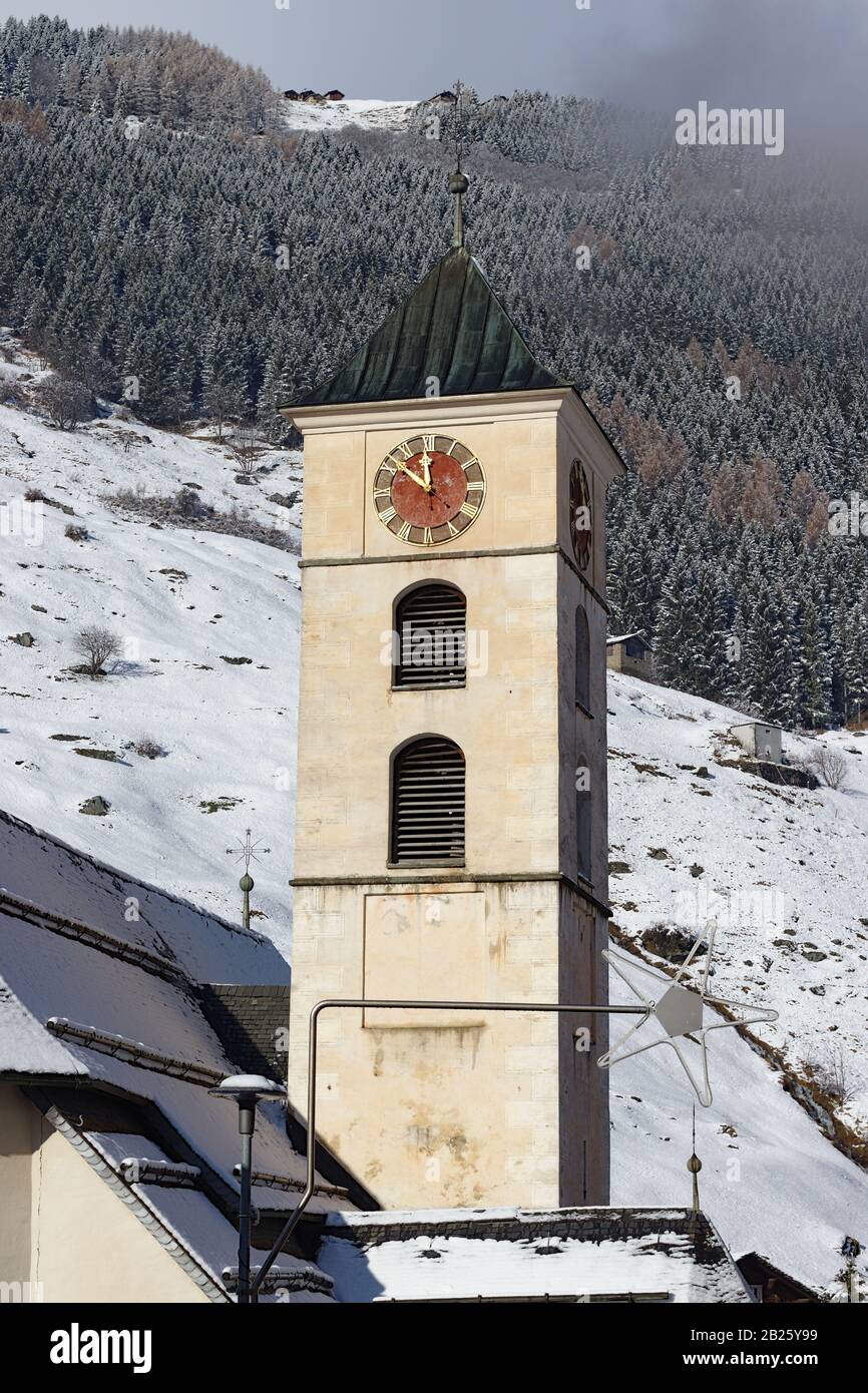 Kirche mit goldenroter Uhr in vals schweiz. Winterlandschaft im Hintergrund Stockfoto