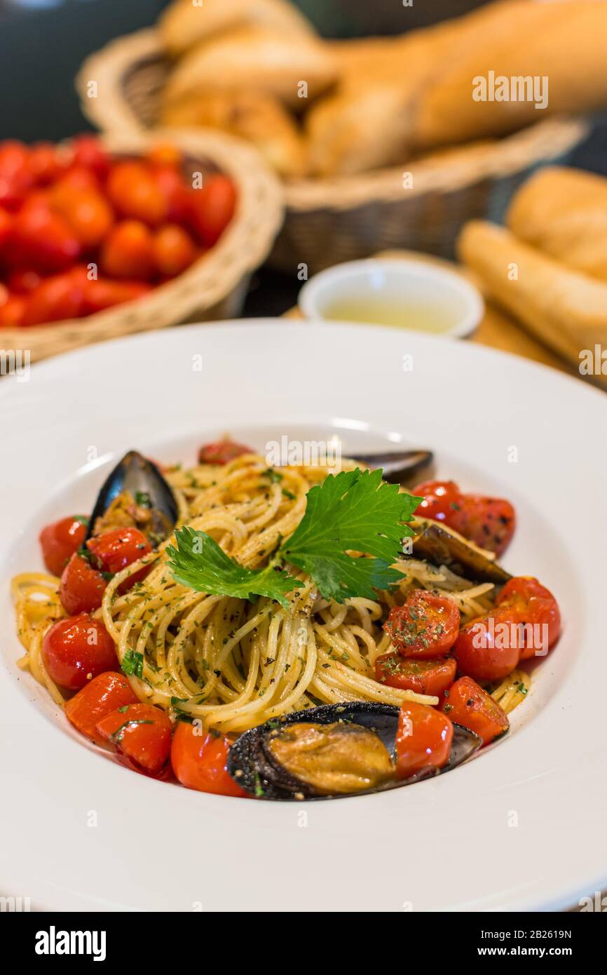 Nahaufnahme von Spaghetti Vongole mit roma-tomaten und Muscheln serviert und auf einem Teller mit Tomaten, Brot und Olivenöl im Hintergrund dekoriert Stockfoto