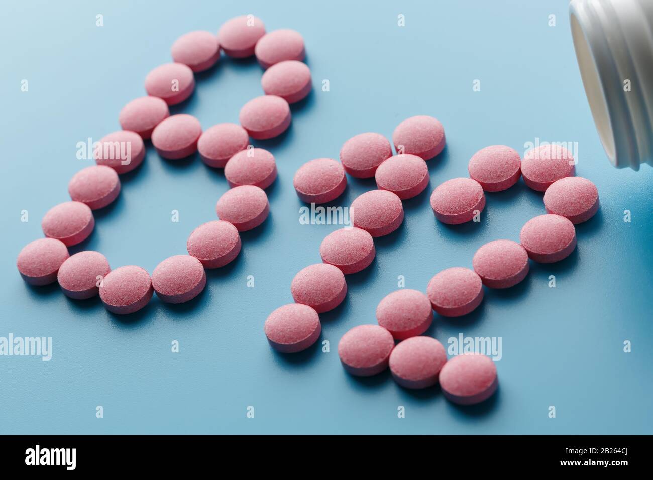 Rosafarbene Pillen in Form des Buchstabens B12 auf blauem Grund, aus einer weißen Dose verschüttet. Konzept der Nahrungsergänzungsmittel Stockfoto