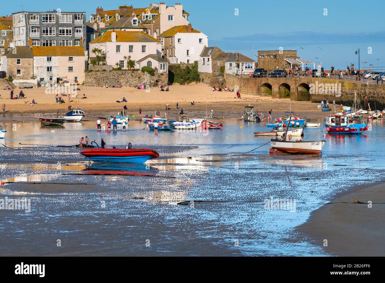 Blick über den Strand von St Ives Harbour zum Smeatons Pier mit Leuten am Strand, Booten im Hafen und Häusern, St Ives, Cornwall, Großbritannien Stockfoto