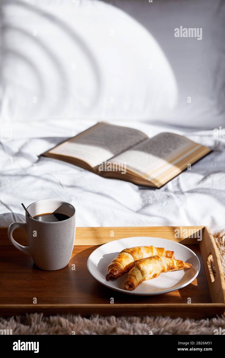 Französische Croissants und schwarzer Kaffee auf dem Tablett im Schlafzimmer zum Frühstück Stockfoto