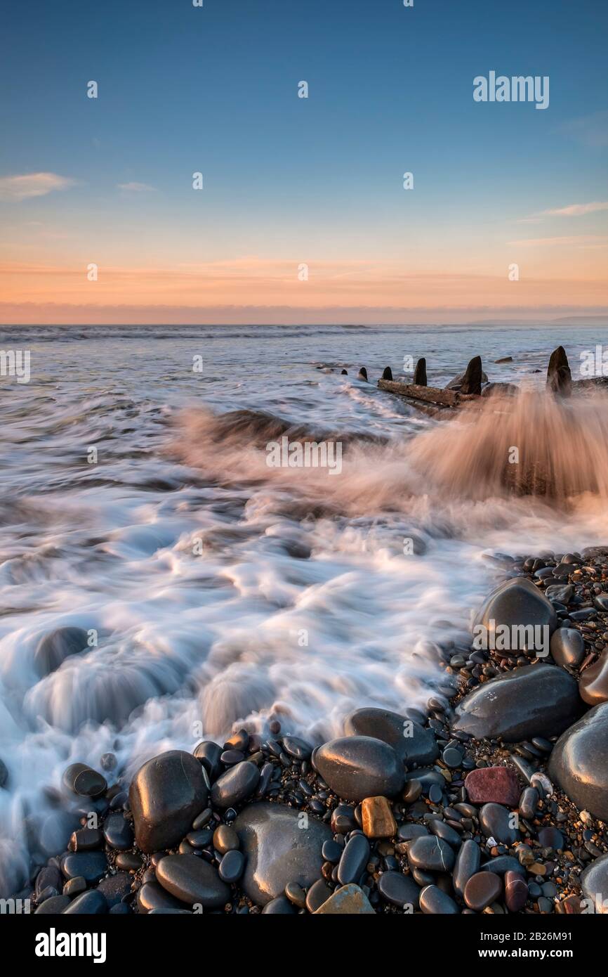 Die Flut, die auf Westward Ho um die Kieselsteine und die Holzmeerschutz-Gabionen spritzt! Strand mit Sonnenuntergang am Horizont, Nord-Devon, Süd-West, Stockfoto
